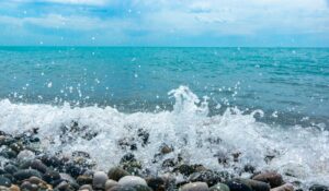 Water splashes against coastal rocks, sending droplets upward, symbolizing emotional release, movement, and renewal