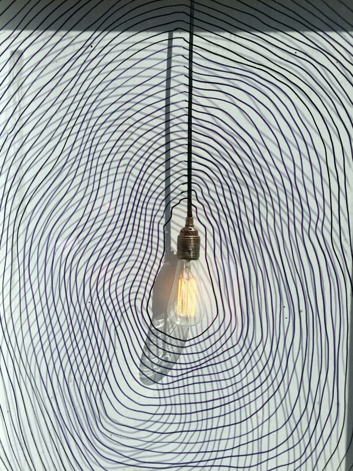 A glowing hanging light bulb centered among warped, contour-like lines illustrates how a CBT therapist in Brooklyn might help someone recognize and reshape distorted thought patterns.