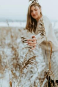 A woman’s hand gently touches dry, wild twigs outdoors during a quie,t reflective moment in nature