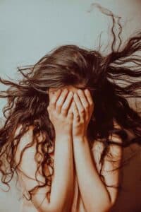 A woman covering her face as the wind blows her hair, expressing overwhelm, vulnerability, and emotional distress.