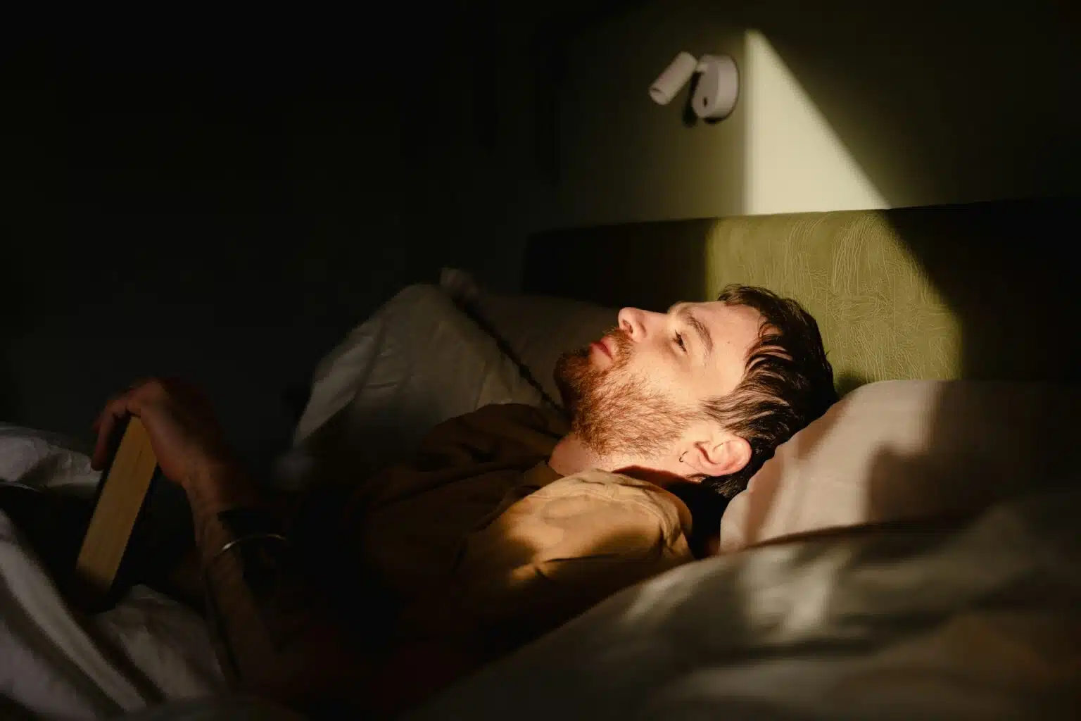A man lying awake in a dark room with light on his face, showing alertness, restlessness, and an inability to fall asleep easily