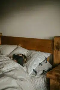 A woman lying in bed, covering her face with her arm, reflecting overwhelming fatigue and the emotional toll of insomnia symptoms