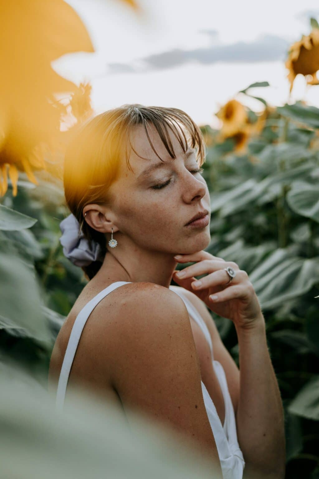 A woman surrounded by sunflowers touching her chin gently, symbolizing self-reflection, growth, and emotional awareness.