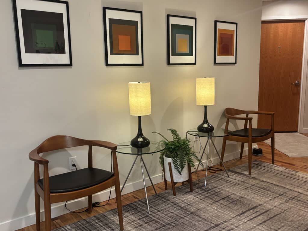 Modern waiting area with two mid-century wooden chairs, glass side tables, matching table lamps,