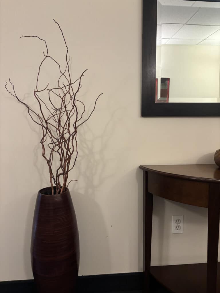 Dark vase with twisted branches beside wood console and mirror minimalist decor.