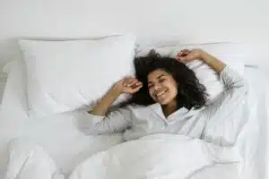A relaxed woman lying comfortably in bed, smiling with eyes closed, suggesting restful sleep and the positive outcome of successful insomnia therapy.