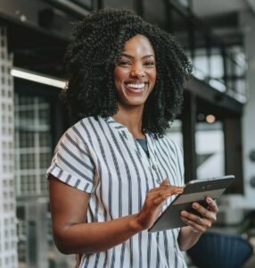 An African American woman holding a tablet, professionally dressed, reflecting confidence, clarity, and personal awareness.
