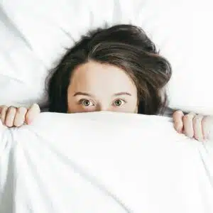 A woman lying in bed, wide awake, under a comforter, reflecting restlessness, anxiety, and difficulty falling asleep at night