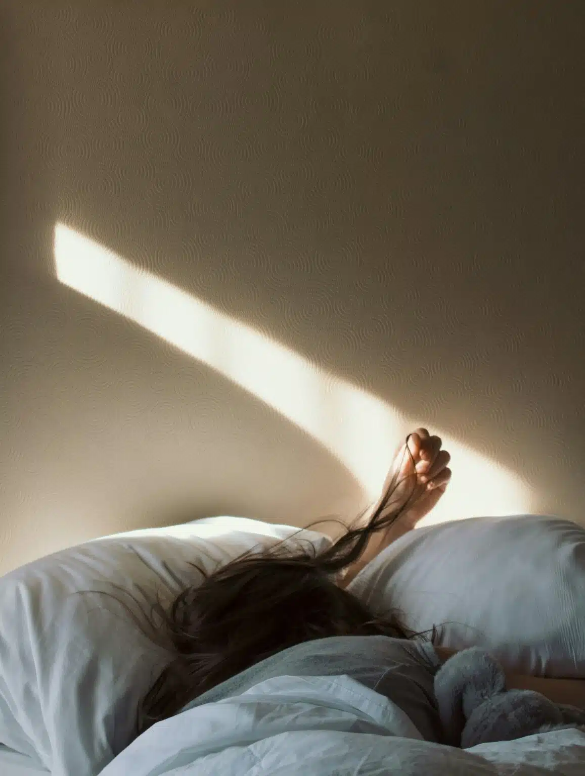 A woman in bed playing with her hair, showing anxiety, rumination, and difficulty relaxing into restful sleep at night