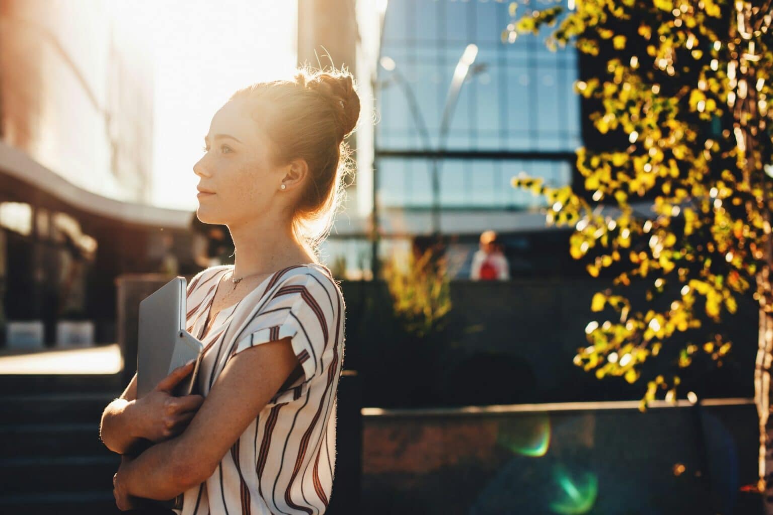 A professional woman holding a laptop at sunset, reflecting productivity, ambition, and balancing external demands.