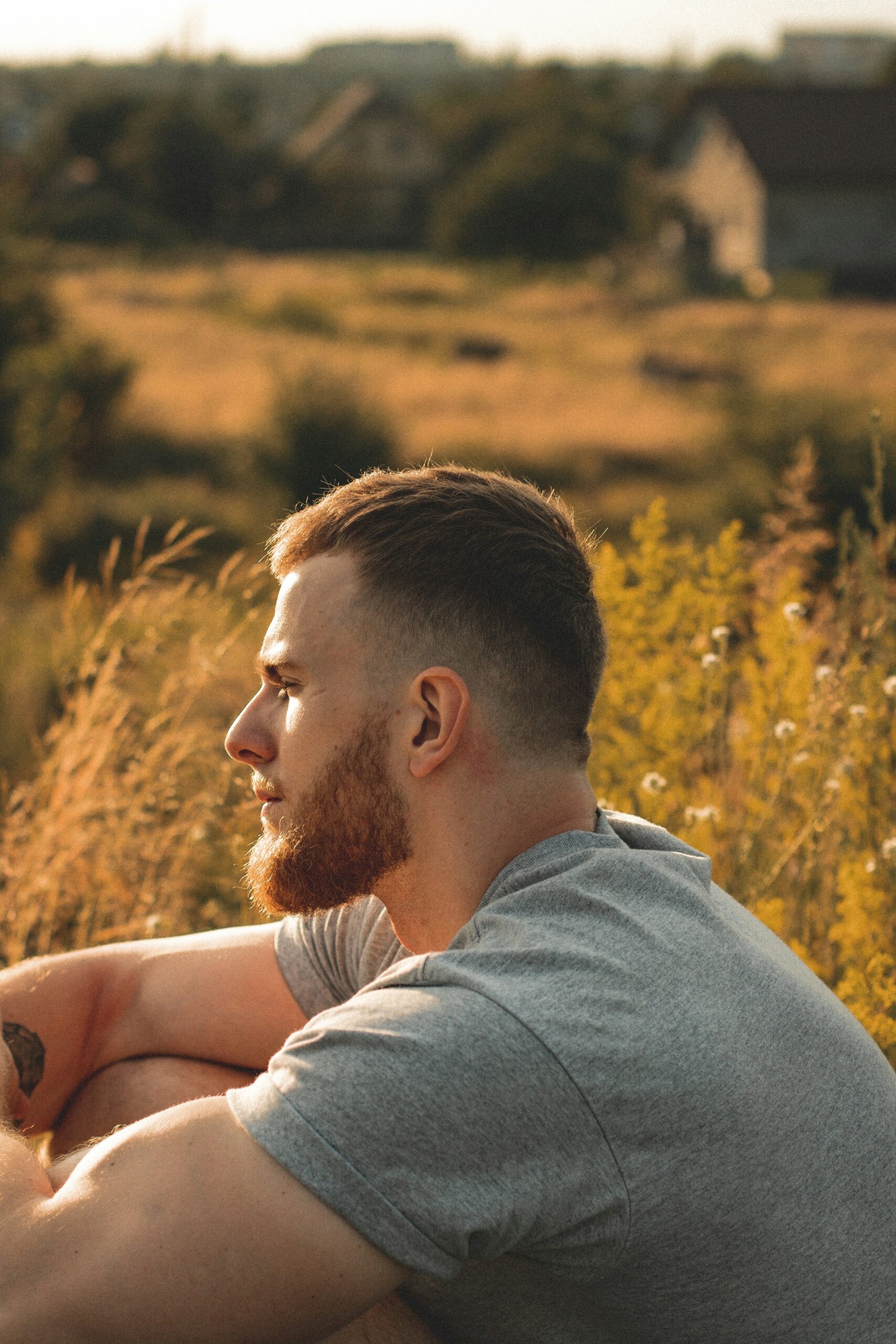 A man sitting in a field with grass and flowers, reflecting contemplation, stillness, and connection to inner thoughts.
