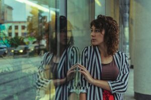 A woman staring into reflective building glass, expressing introspection, self-awareness, and inner emotional tension.