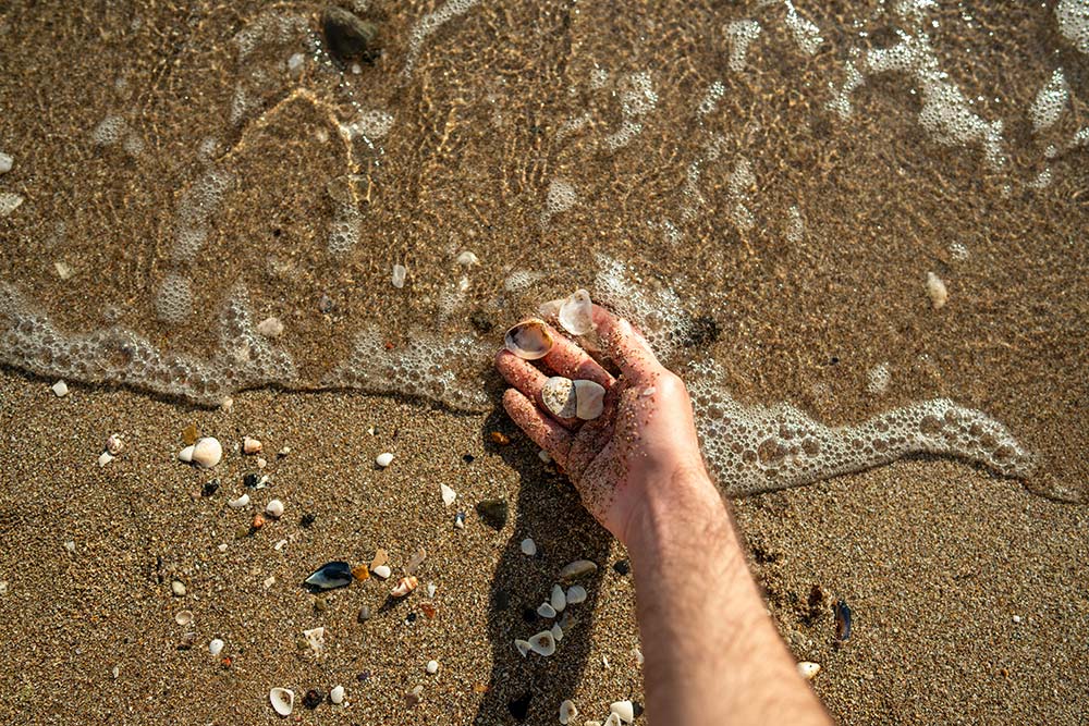 A hand holds pebbles on the sandy beach