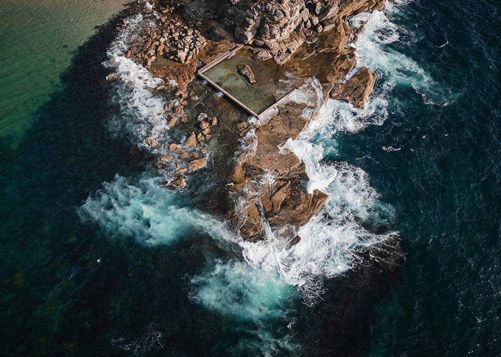 aerial view of an ocean pool surrounded by crashing waves