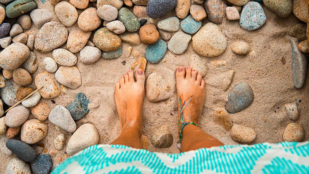 feet standing on sand and pebbles at the beach
