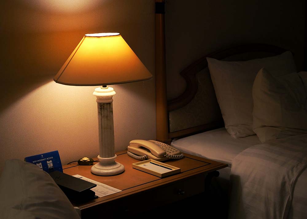 A lamp on a nightstand beside a bed.
